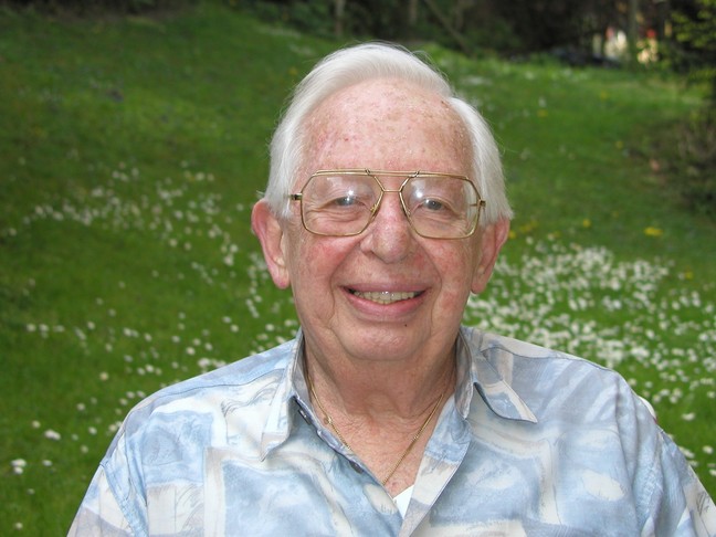 An older Frank Alper laughing warmly in a sunlit garden.